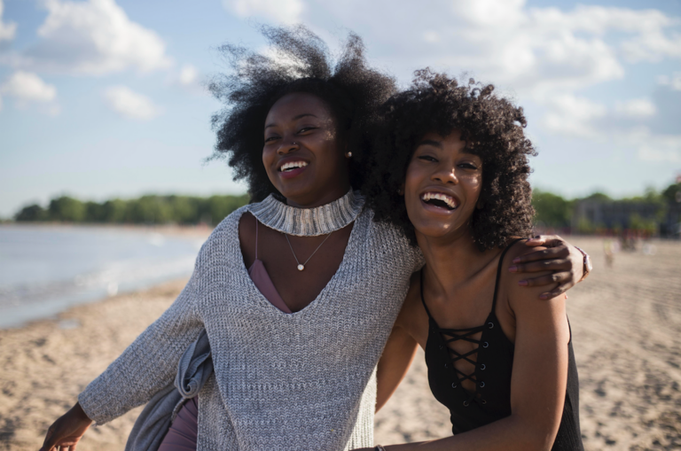 two women smiling and hugging on beach
