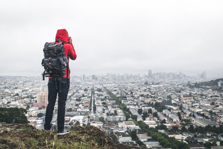 man taking scenic photo of city from hills above